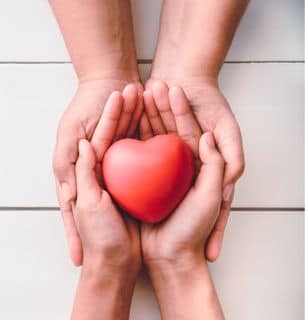 hands reaching across the table, cupping one another with a heart on top