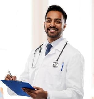 Male doctor, smiling, while writing on clipboard